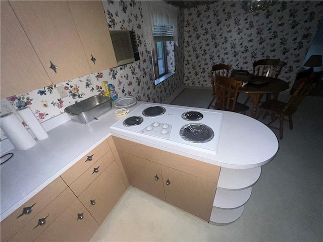 kitchen featuring white electric stovetop, light countertops, light brown cabinetry, a peninsula, and wallpapered walls