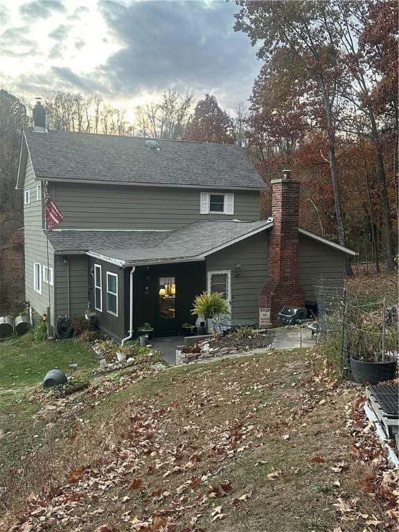 rear view of house with a shingled roof, a patio area, and a chimney