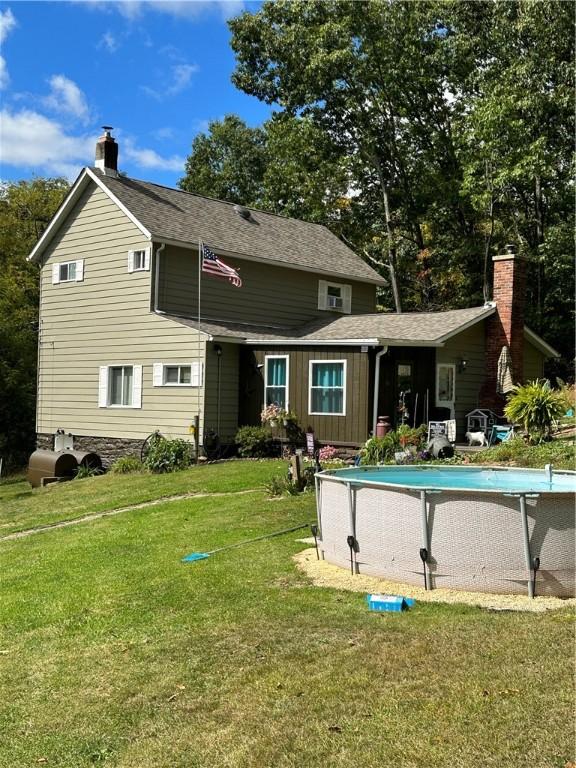 back of property featuring an outdoor pool, roof with shingles, a yard, and a chimney