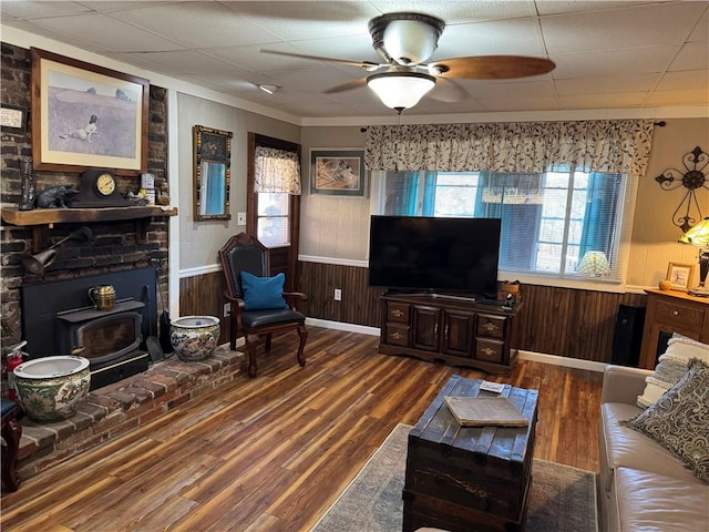 living area with wainscoting, wood finished floors, a wood stove, and a healthy amount of sunlight