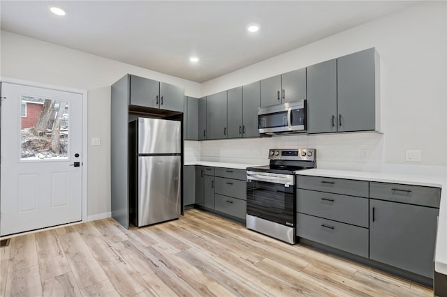 kitchen with stainless steel appliances, decorative backsplash, light wood-style flooring, and gray cabinetry