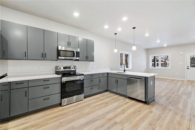 kitchen with stainless steel appliances, a peninsula, gray cabinets, light wood finished floors, and tasteful backsplash