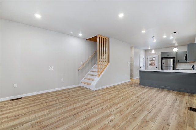 unfurnished living room with stairway, recessed lighting, light wood-style flooring, and baseboards