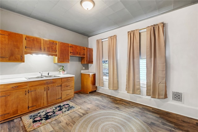 kitchen featuring wood finished floors, brown cabinetry, a sink, and visible vents