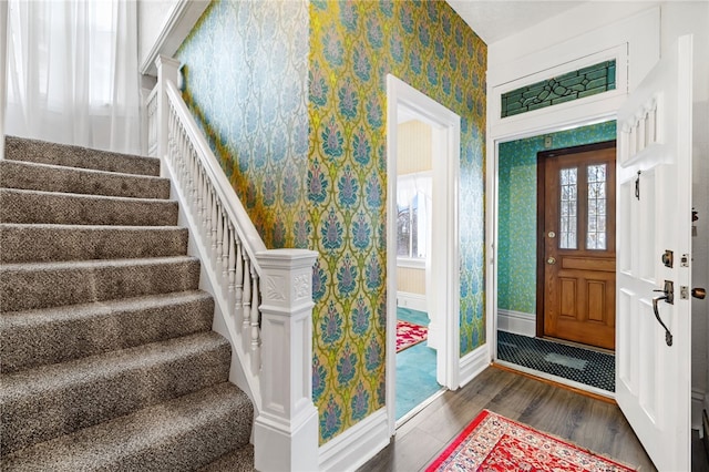 entryway featuring wallpapered walls, stairs, baseboards, and wood finished floors