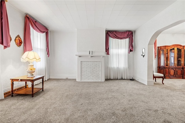 carpeted living room featuring baseboards and arched walkways