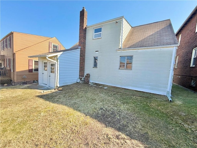 rear view of property featuring a shingled roof, a lawn, and a chimney