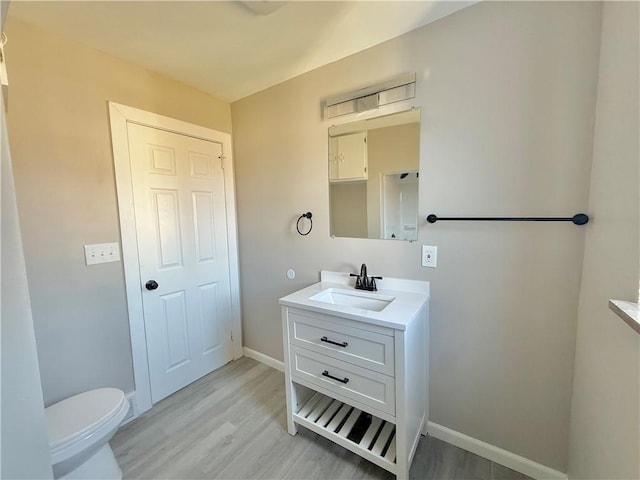 bathroom featuring toilet, baseboards, wood finished floors, and vanity