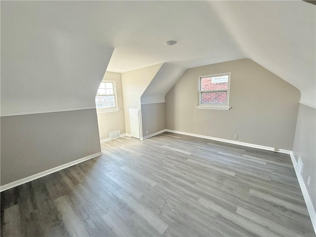 bonus room featuring baseboards, visible vents, vaulted ceiling, and wood finished floors