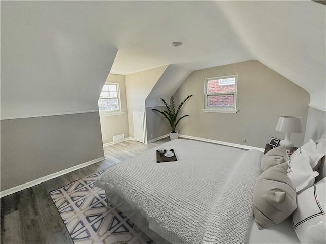 bedroom featuring visible vents, baseboards, lofted ceiling, and wood finished floors