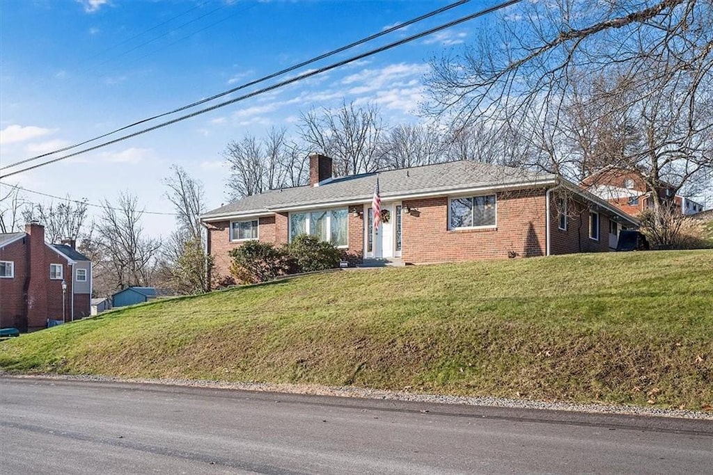 single story home featuring a chimney, a front lawn, and brick siding