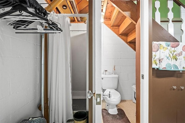 bathroom featuring toilet and concrete block wall