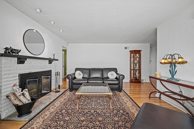 living area featuring baseboards, visible vents, wood finished floors, and a glass covered fireplace