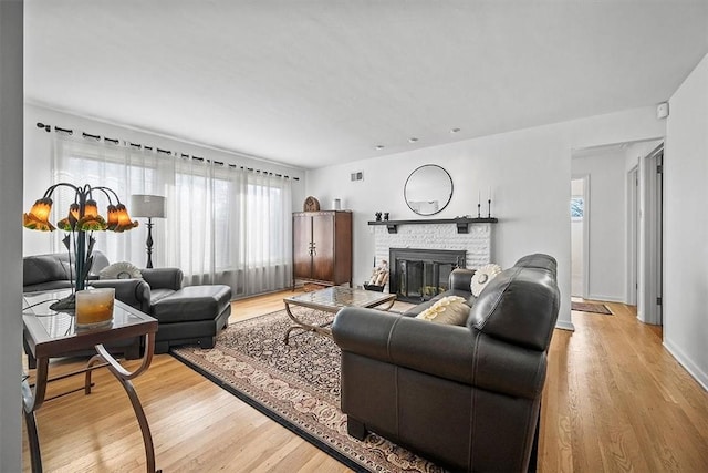 living room featuring visible vents, a glass covered fireplace, light wood-style flooring, and baseboards