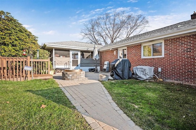 back of house featuring a yard, brick siding, a patio area, and a sunroom