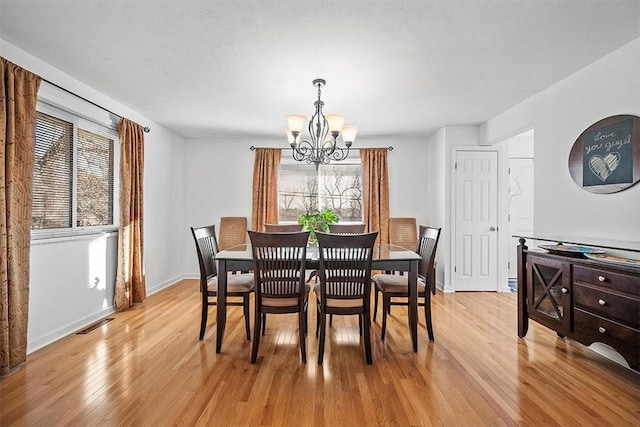 dining space with a textured ceiling, visible vents, baseboards, light wood-style floors, and an inviting chandelier