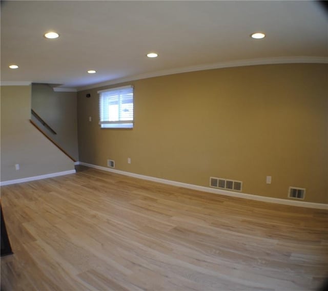 below grade area featuring baseboards, light wood-style flooring, visible vents, and crown molding