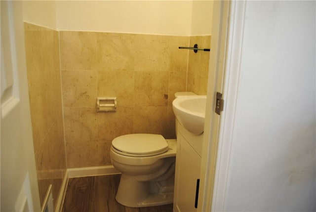 half bathroom featuring toilet, vanity, tile walls, and wood finished floors