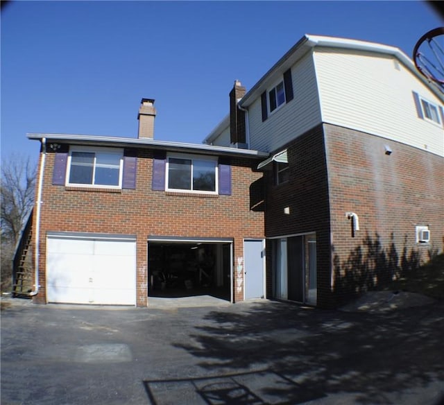 back of house featuring a garage, brick siding, a chimney, and aphalt driveway