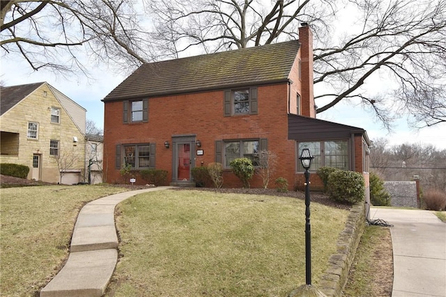 colonial inspired home with a chimney, a front lawn, and brick siding