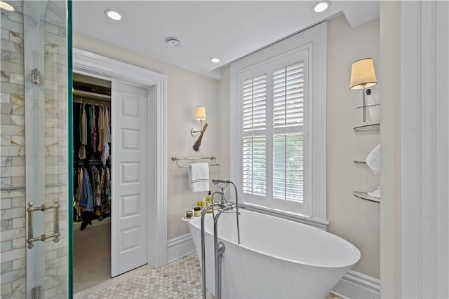 bathroom featuring a spacious closet, a soaking tub, a shower stall, and baseboards