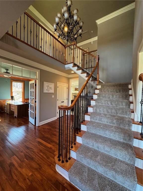 stairway featuring a notable chandelier, crown molding, a towering ceiling, and wood finished floors