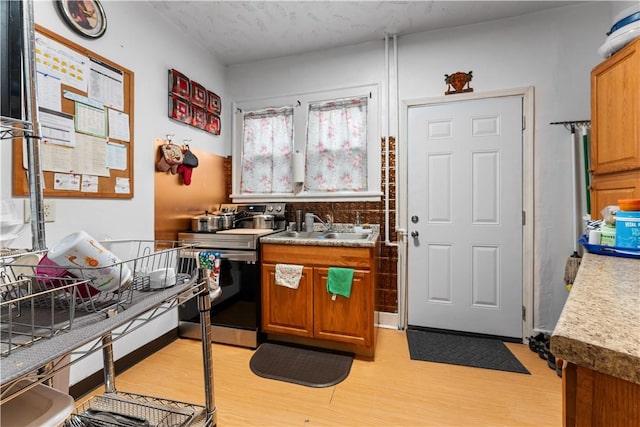 kitchen with light wood-style flooring, stainless steel electric range, brown cabinetry, and a sink