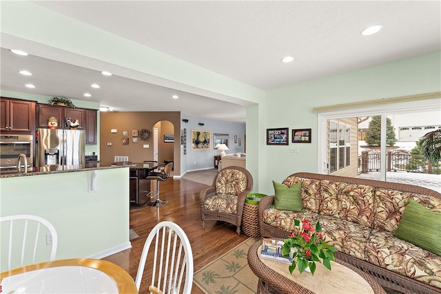 living area featuring arched walkways, dark wood-type flooring, and recessed lighting