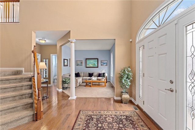 entrance foyer featuring stairway, a high ceiling, light wood finished floors, and ornate columns