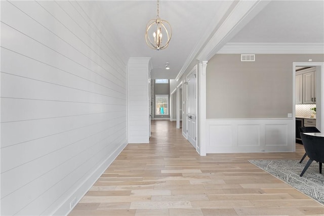 hallway featuring a notable chandelier, visible vents, a decorative wall, light wood-style floors, and ornamental molding