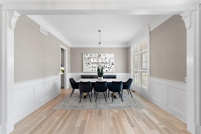 dining room featuring light wood-style floors, a wainscoted wall, visible vents, and crown molding