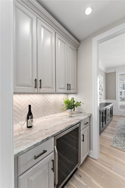 bar featuring light wood-type flooring, wine cooler, decorative backsplash, and crown molding