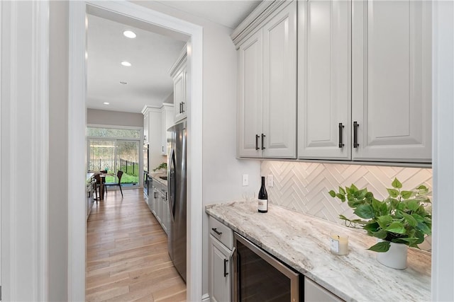 bar with decorative backsplash, wine cooler, freestanding refrigerator, a bar, and light wood-style floors