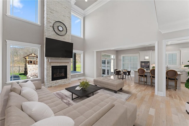 living area with light wood finished floors, baseboards, a towering ceiling, ornamental molding, and a fireplace