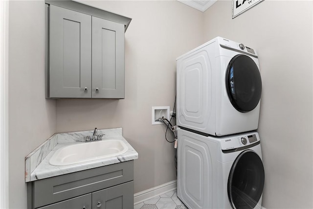 washroom featuring cabinet space, a sink, stacked washer and clothes dryer, and baseboards