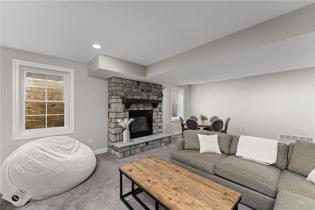 living area featuring carpet, a healthy amount of sunlight, a stone fireplace, and baseboards