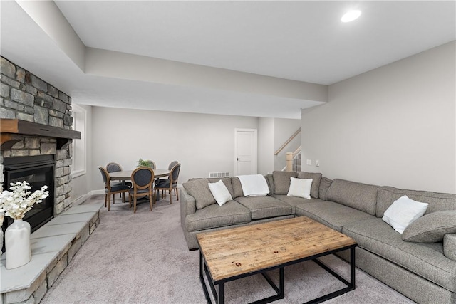 living area with light carpet, stairs, visible vents, and a stone fireplace