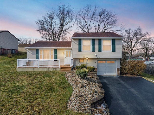 split level home featuring a garage, aphalt driveway, and a yard