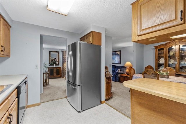 kitchen featuring a textured ceiling, dishwashing machine, light carpet, light countertops, and freestanding refrigerator