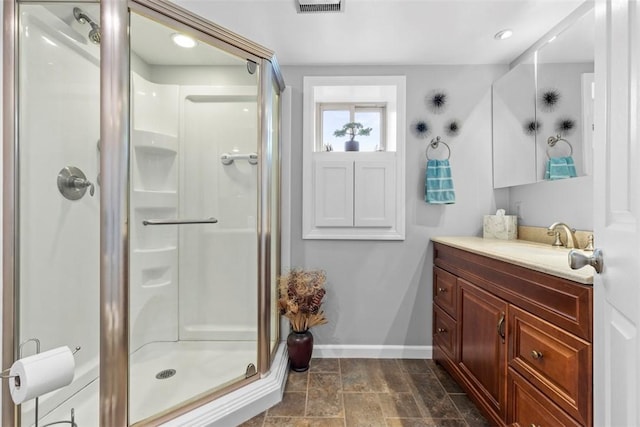 full bath featuring a stall shower, stone finish floor, vanity, and baseboards