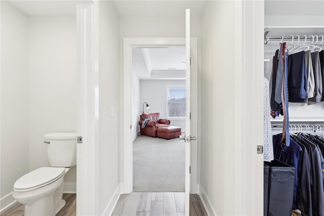 interior space featuring wood finished floors, a walk in closet, toilet, and baseboards