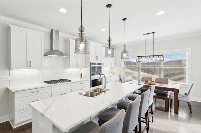 kitchen featuring double oven, ornamental molding, a sink, wall chimney range hood, and gas cooktop