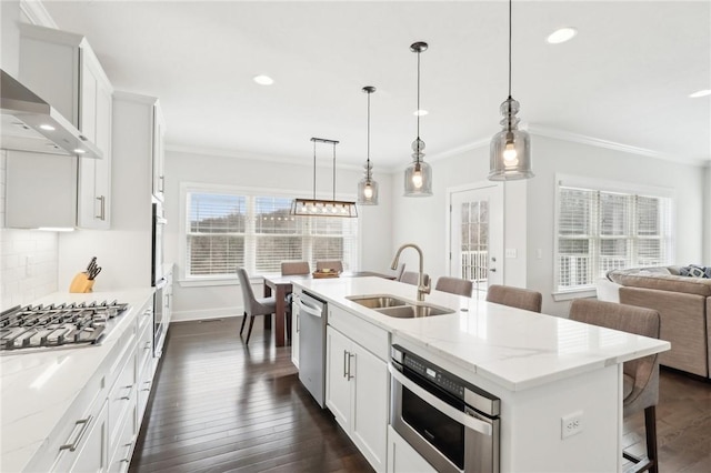 kitchen with ornamental molding, wall chimney range hood, a sink, and appliances with stainless steel finishes