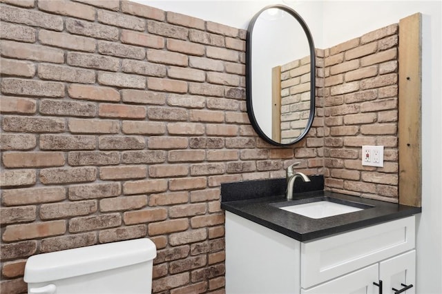 bathroom with toilet, brick wall, and vanity