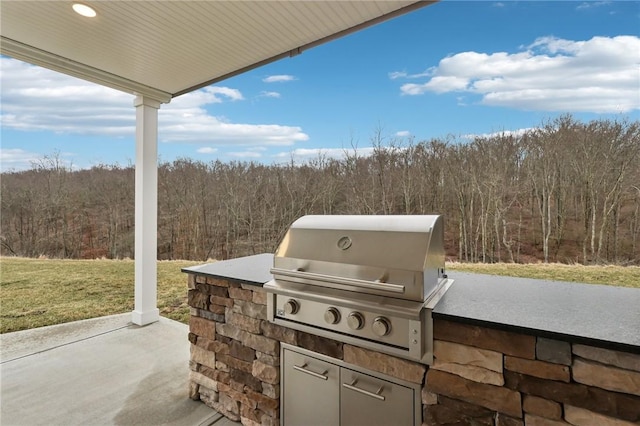 view of patio with a grill, an outdoor kitchen, and a forest view