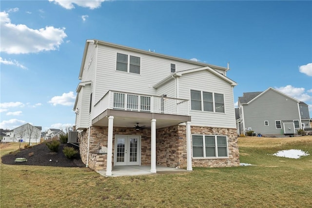 rear view of house with a ceiling fan, french doors, stone siding, a yard, and a patio area