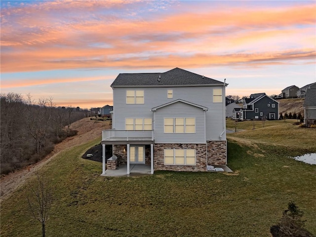 back of property at dusk with a patio area, a yard, stone siding, and french doors