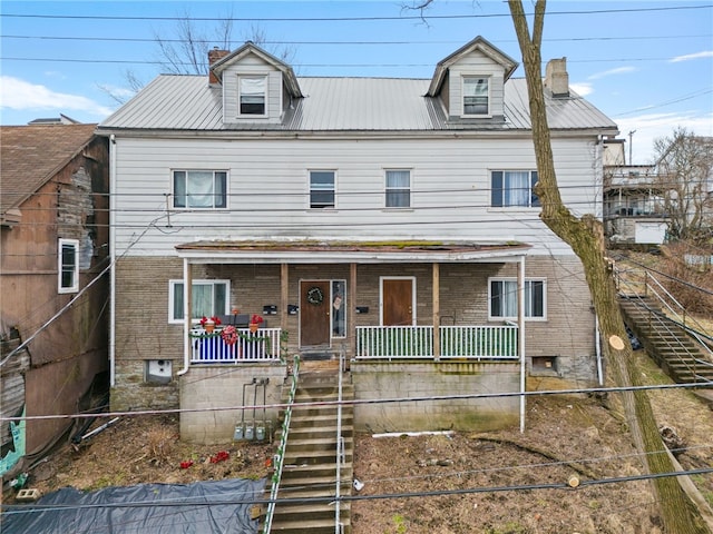 view of front of property featuring brick siding, a chimney, a porch, metal roof, and stairs