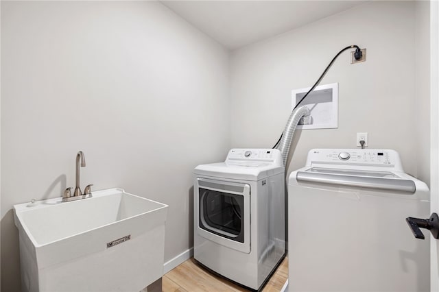 laundry area featuring laundry area, light wood finished floors, baseboards, independent washer and dryer, and a sink