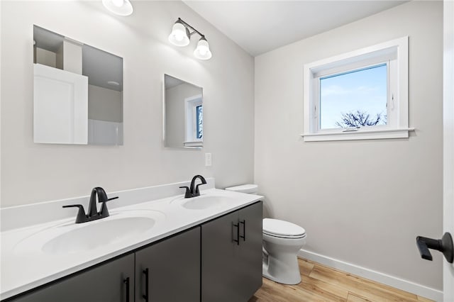 bathroom with double vanity, a sink, toilet, and wood finished floors